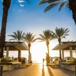 photo of woman and toddler standing near green leaf palm trees under clear blue sky